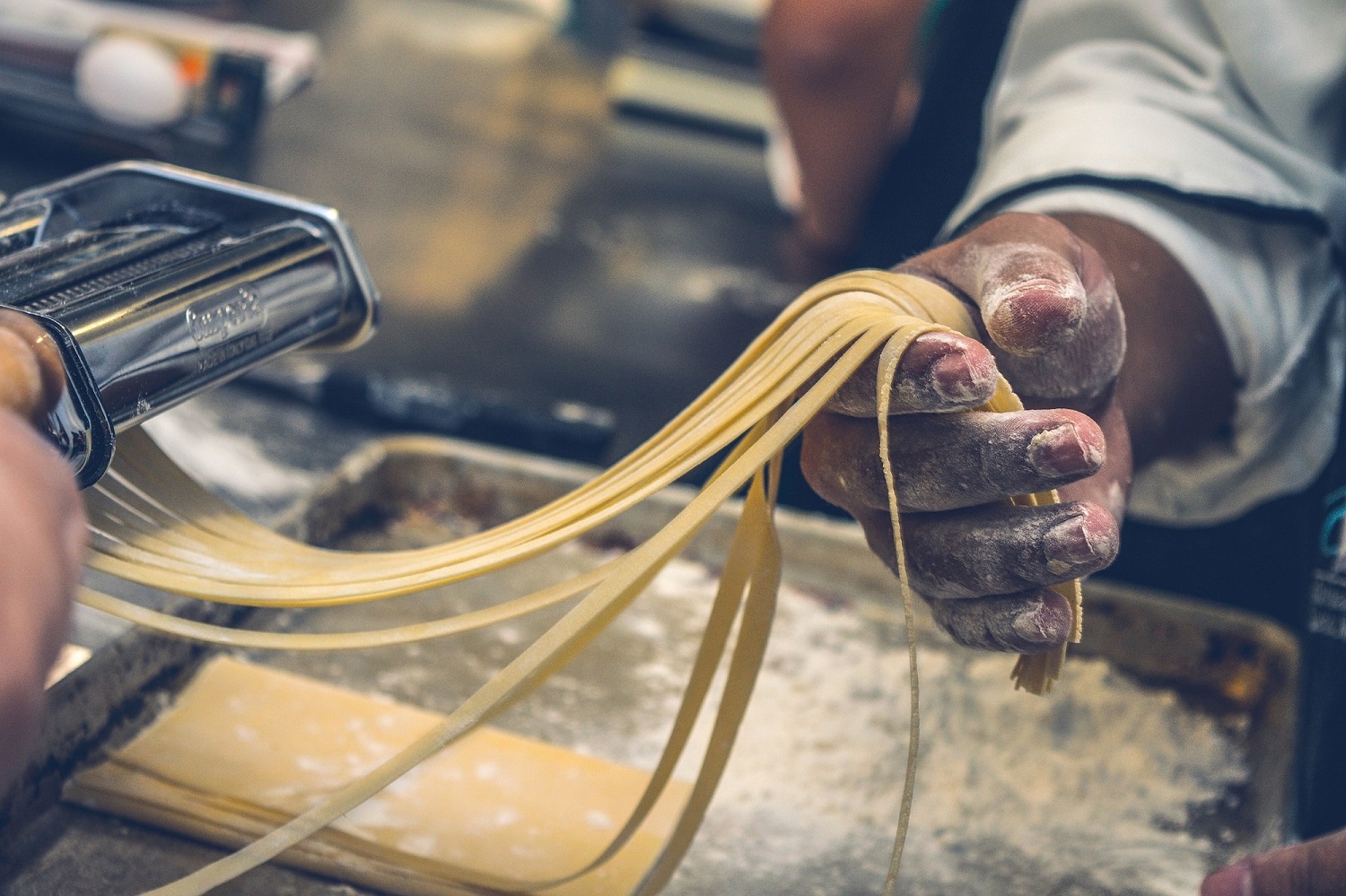 Pasta Maschine, Hand hält Pasta die gerade zu Tagliatelle geschnitten wurde