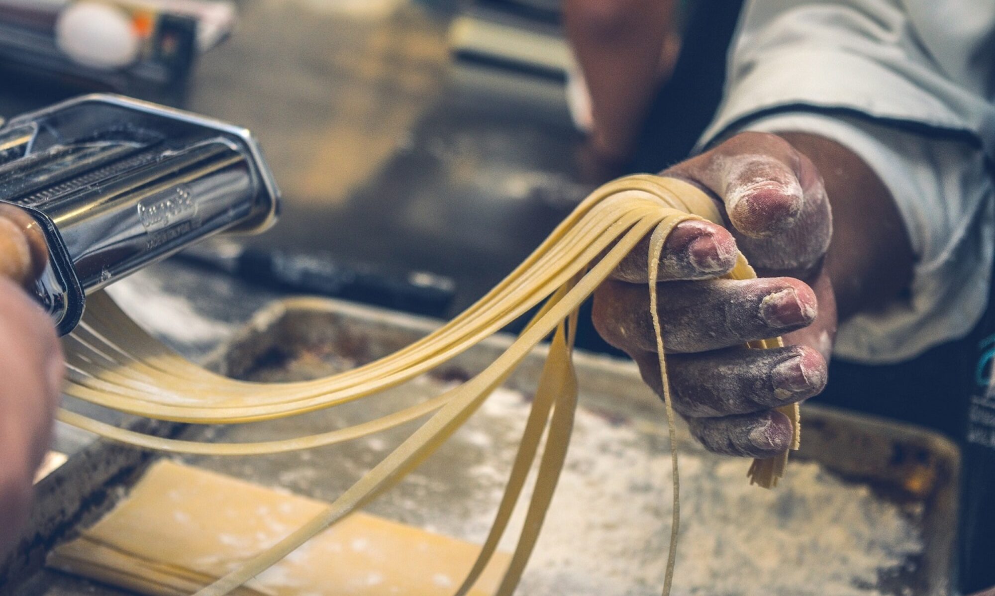 Pasta Maschine, Hand hält Pasta die gerade zu Tagliatelle geschnitten wurde